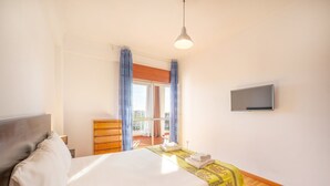 A bedroom with a bed, a wooden dresser, a TV, and a balcony with curtains. - GuestReady - Charming stay with a terrace (Cascais)