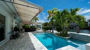 A swimming pool with a covered patio area, palm trees, and a waterfront view. - Casa Flamingo Intracoastal Heated Pool (Fort Lauderdale)