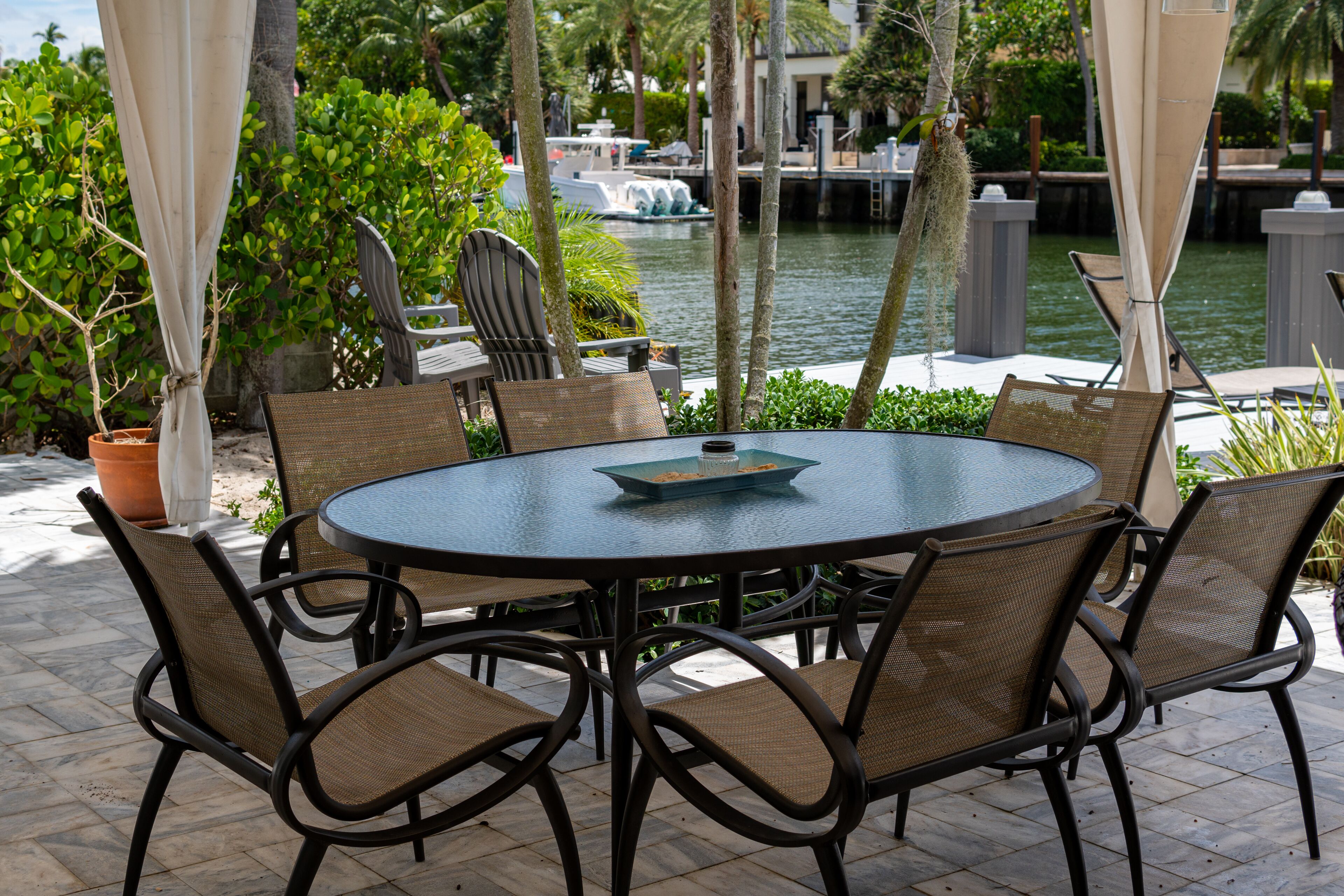 An outdoor patio with a round table and chairs, surrounded by potted plants and a view of a water body.