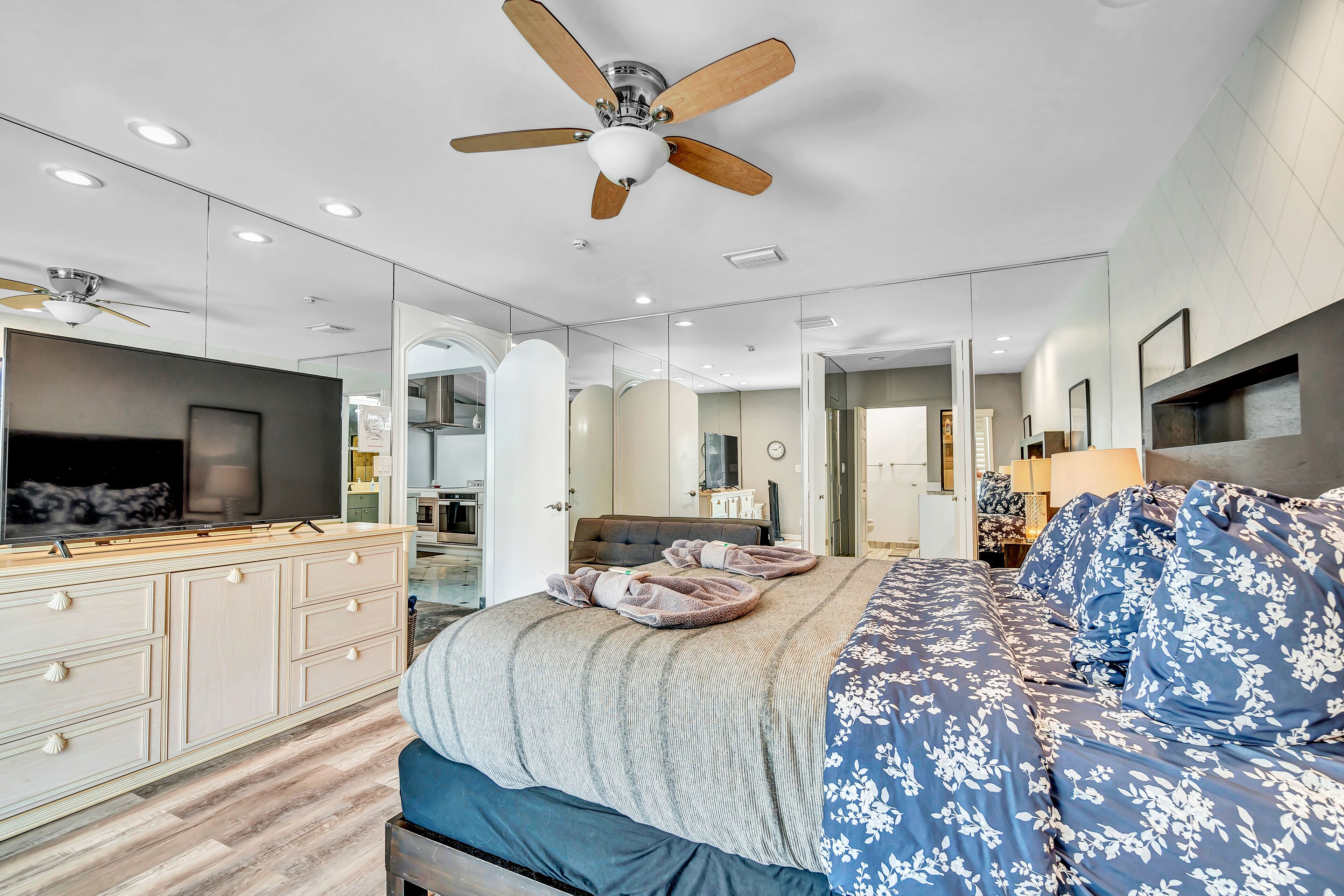 A modern bedroom with a large bed, a ceiling fan, a TV, and a dresser.