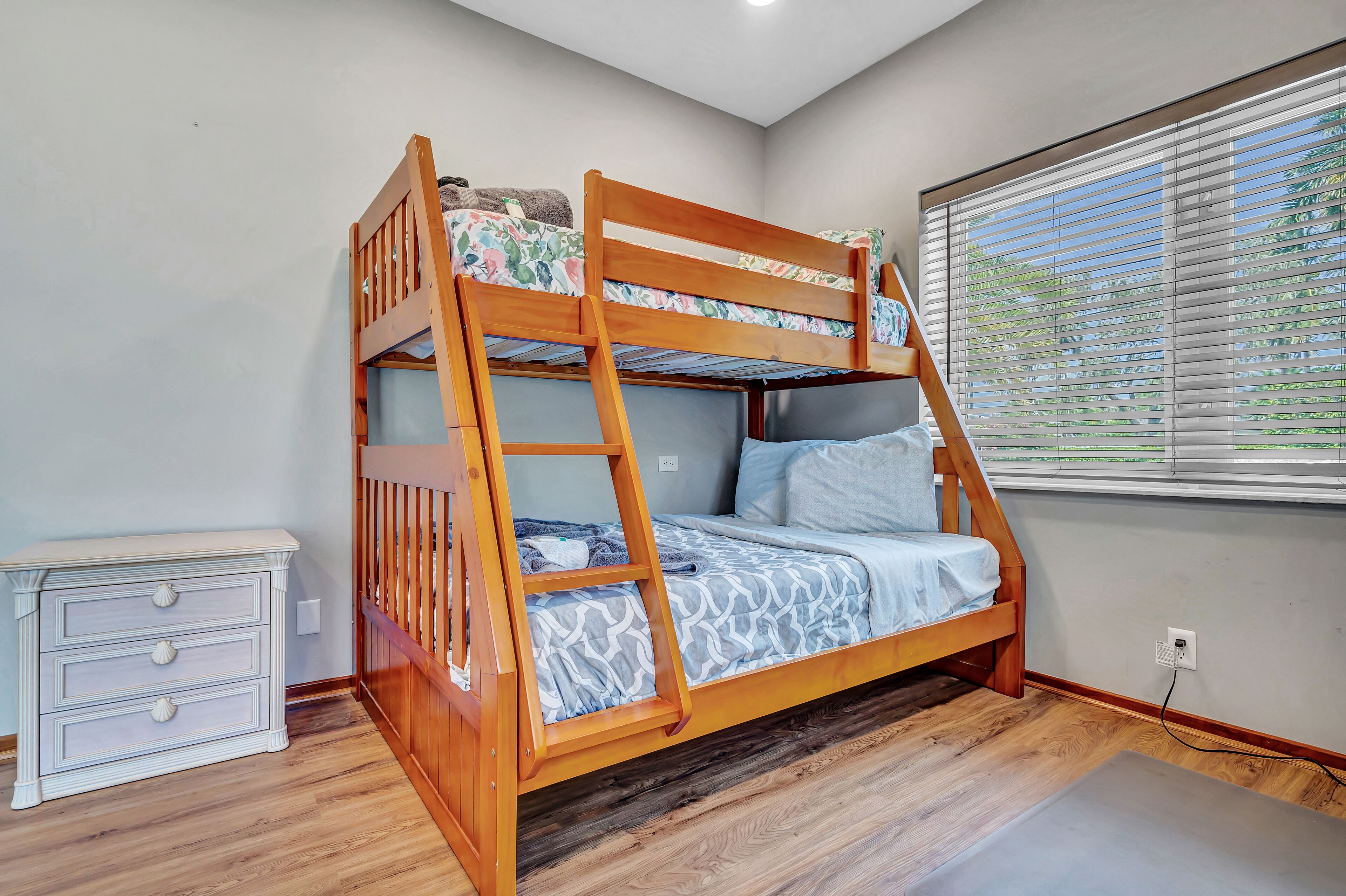 A bunk bed with a ladder, a bedside table, and a window with blinds.