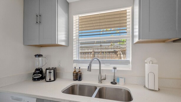 Eine Küche mit einem doppelten Spülbecken, einem Toaster, einem Mixer, einem Wasserhahn und einem Fenster mit Jalousien.
