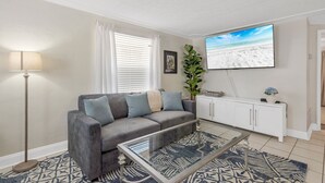 Ein Wohnzimmer mit einer Couch, einem Couchtisch, einem Fernseher, einer Pflanze und einem Schrank.