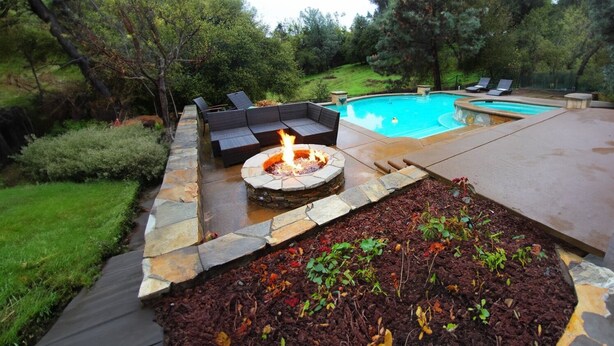 Un patio trasero con un pozo de fuego de piedra, una piscina y mobiliario de exterior.