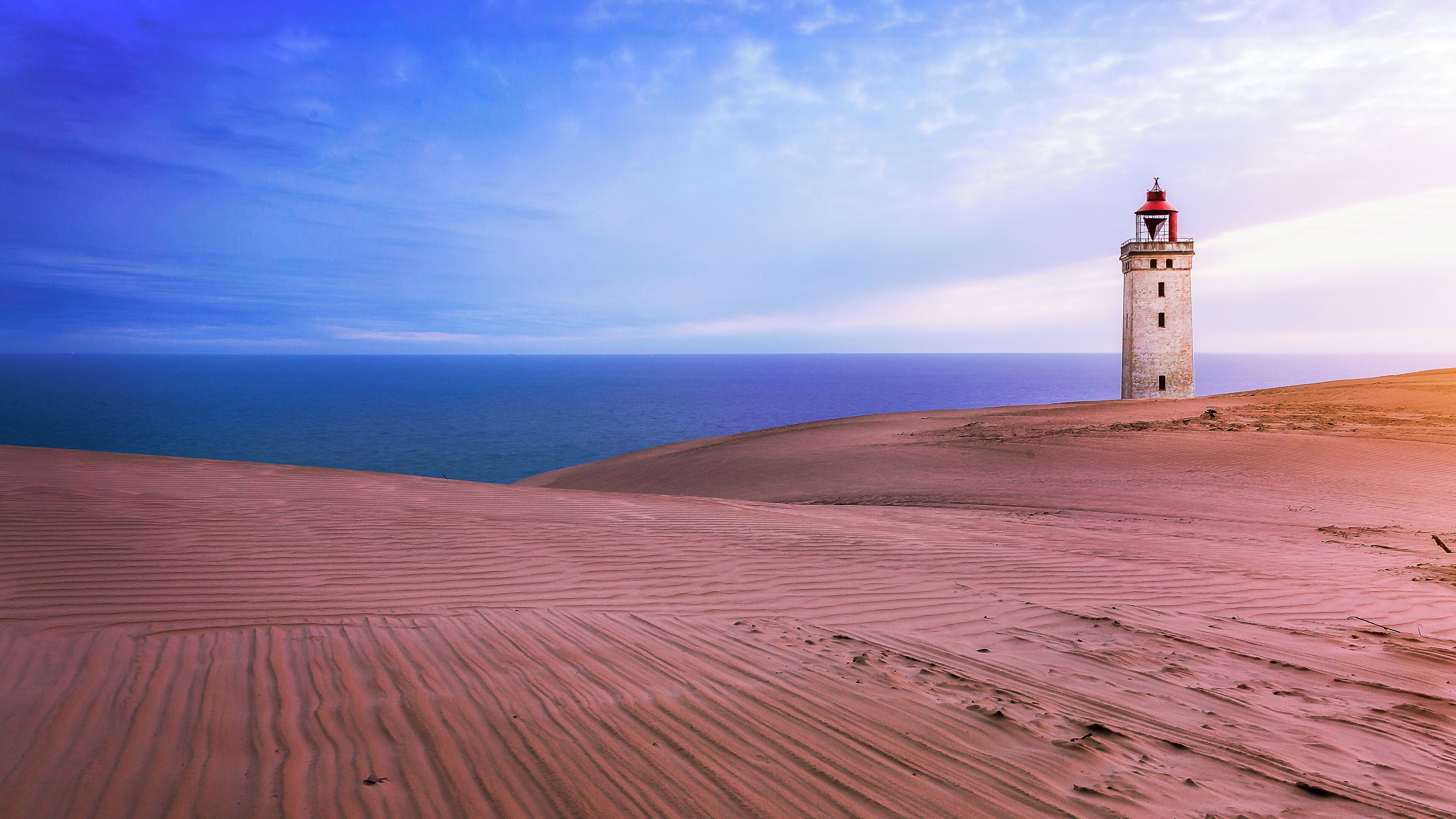 Eine Küstenlandschaft mit einem Leuchtturm auf einer Sanddüne, mit Blick auf das Meer.