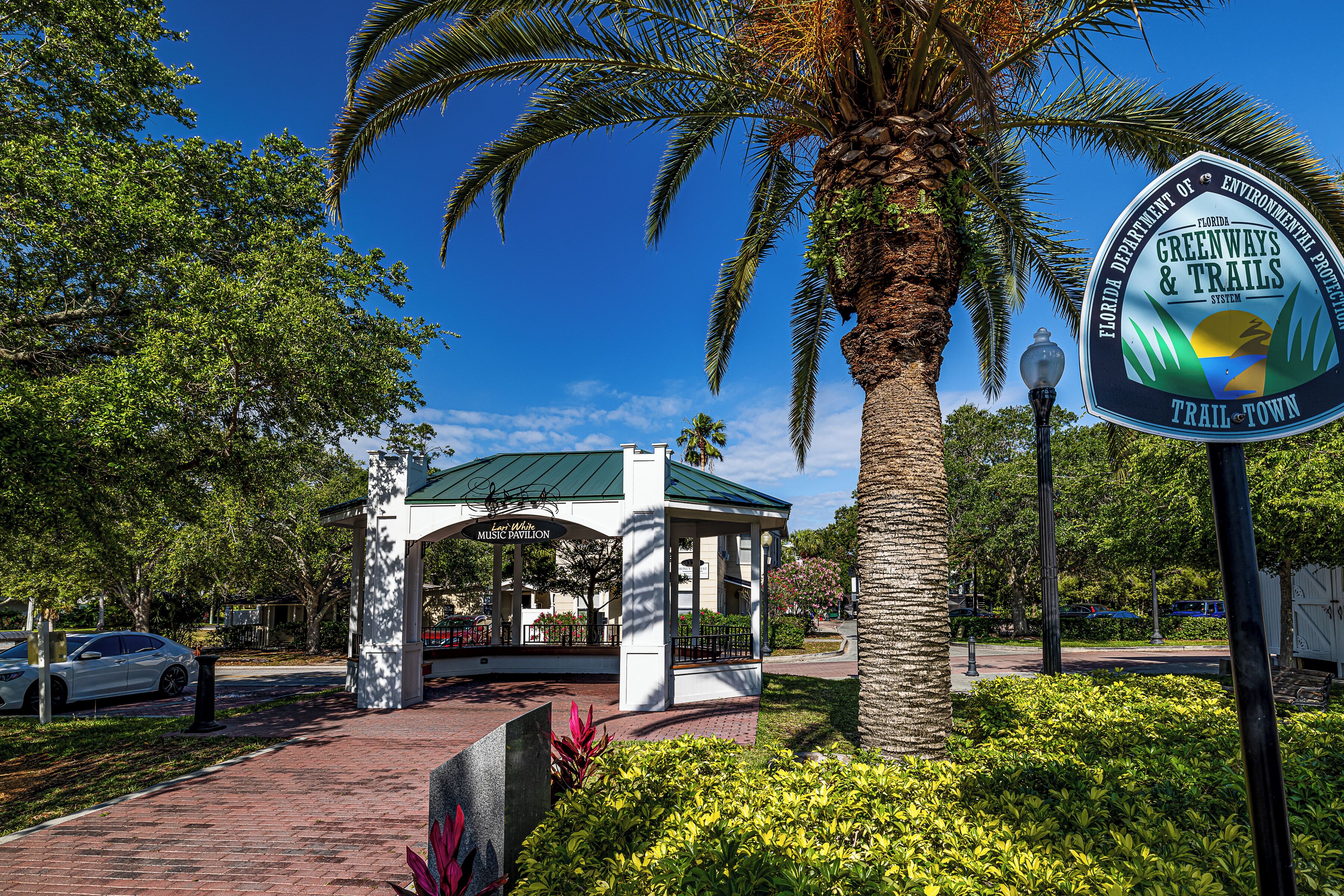 A gazebo with a green roof, surrounded by palm trees and well-maintained bushes.