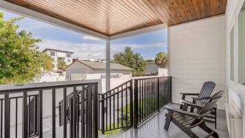 A covered balcony with a wooden ceiling, a black metal railing, and a Adirondack chair.