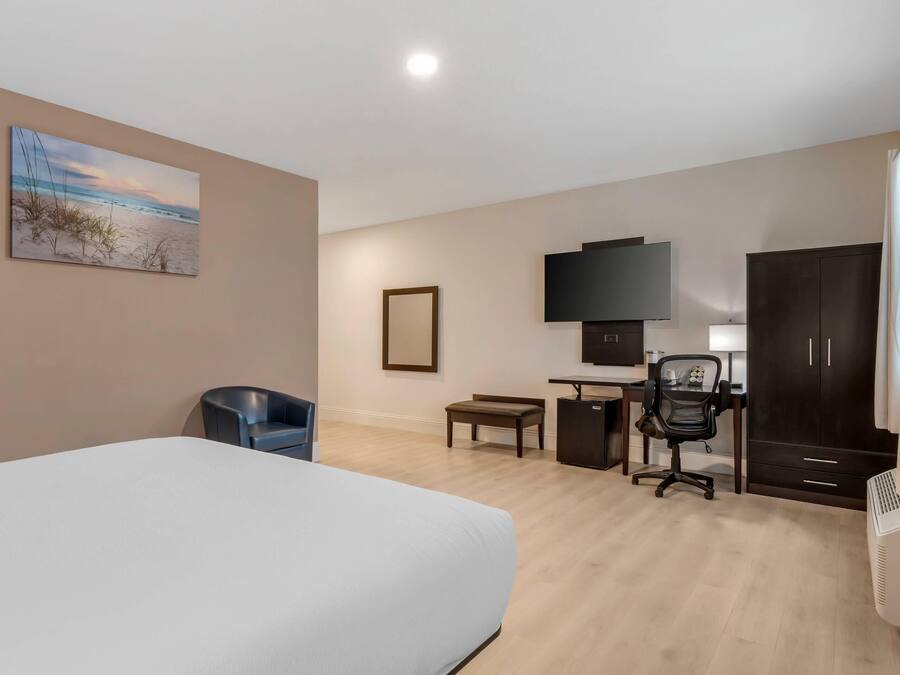 Een hotelkamer met een bed, bureau, stoel, televisie, kledingkast en een schilderij aan de muur.