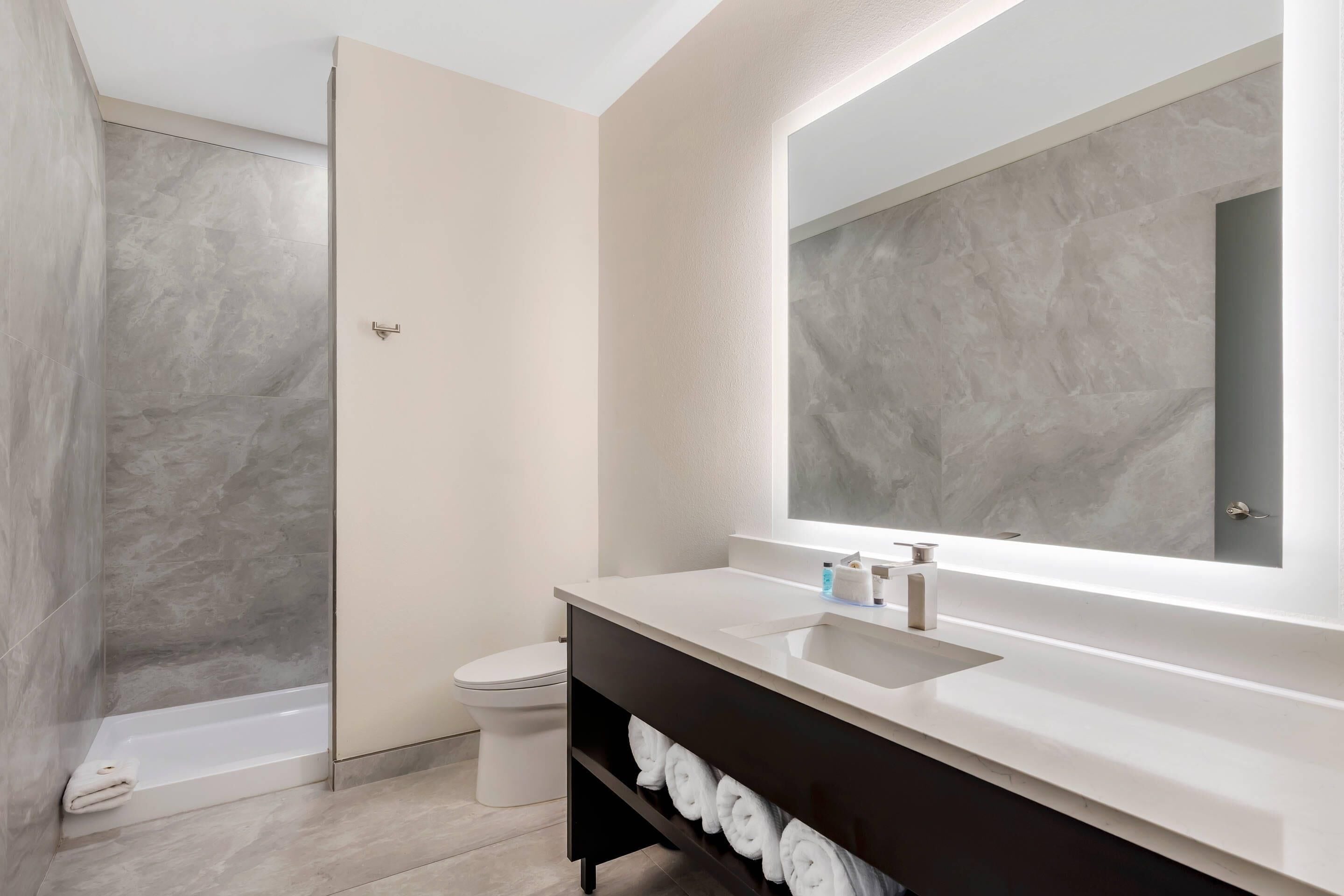 A modern bathroom with a walk-in shower, a toilet, a vanity with a mirror, and a shelf with towels.