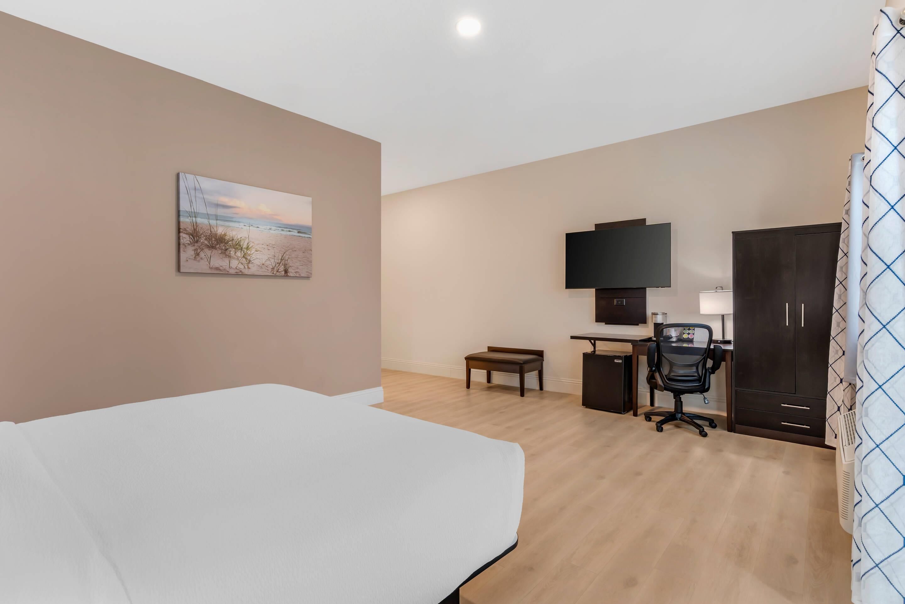 A hotel room with a bed, desk, chair, TV, and a painting on the wall.