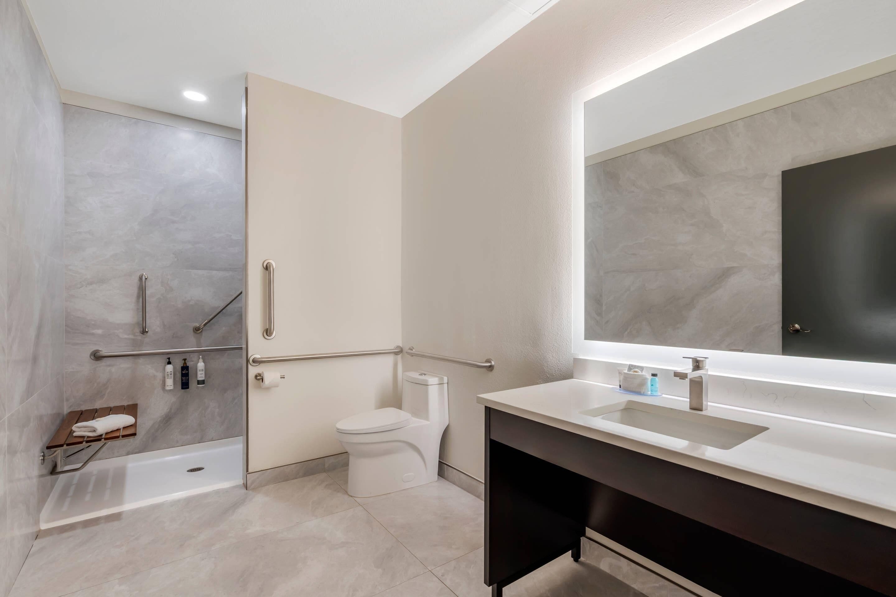 Un baño moderno con ducha, inodoro, tocador y un espejo grande.