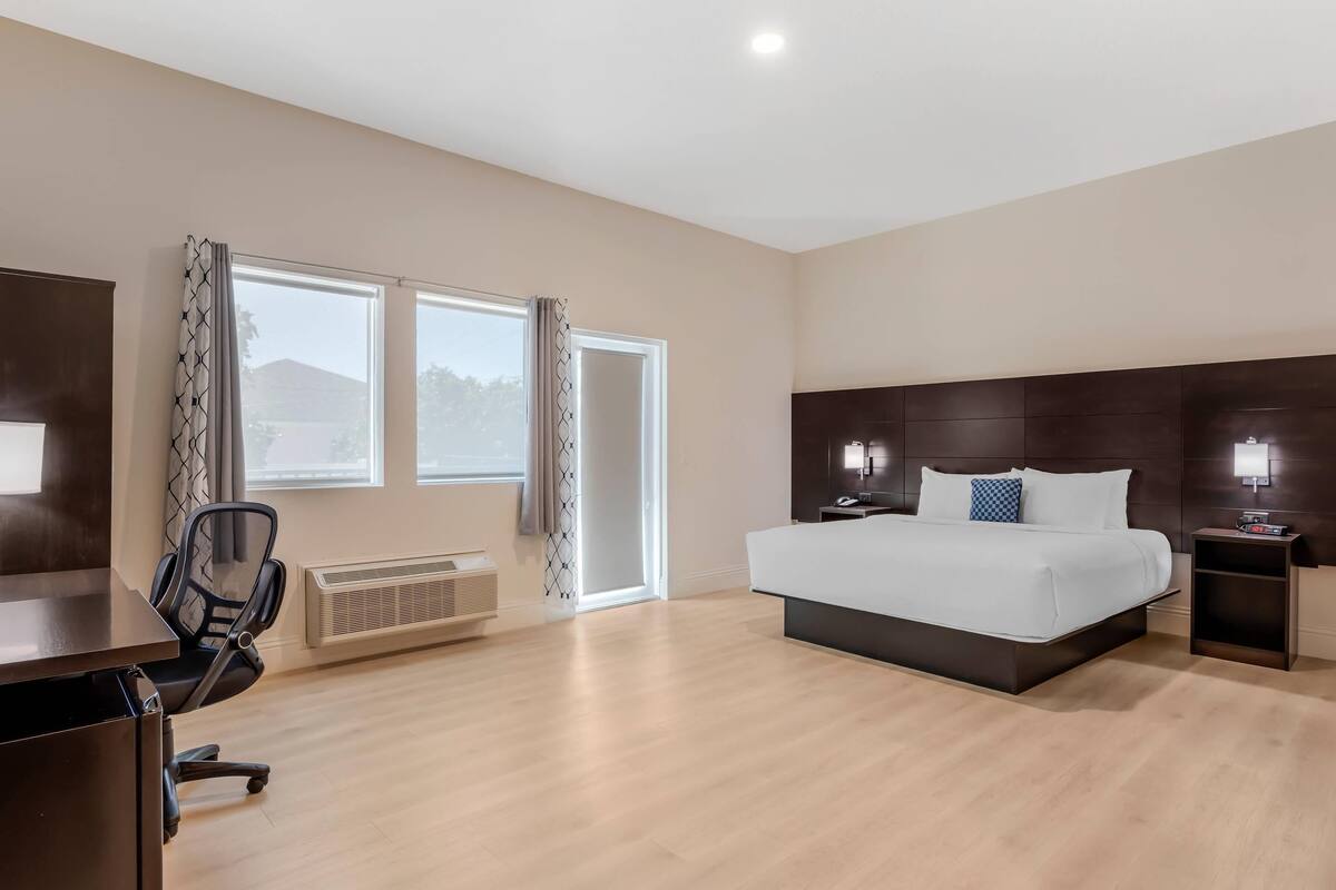A hotel room with a large bed, a desk with a chair, and a window with curtains.