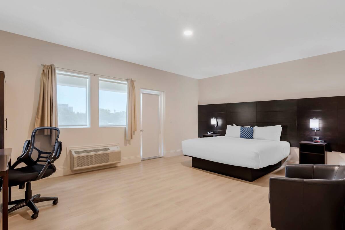 A hotel room with a large bed, a desk, a chair, a heater, and a window with curtains.