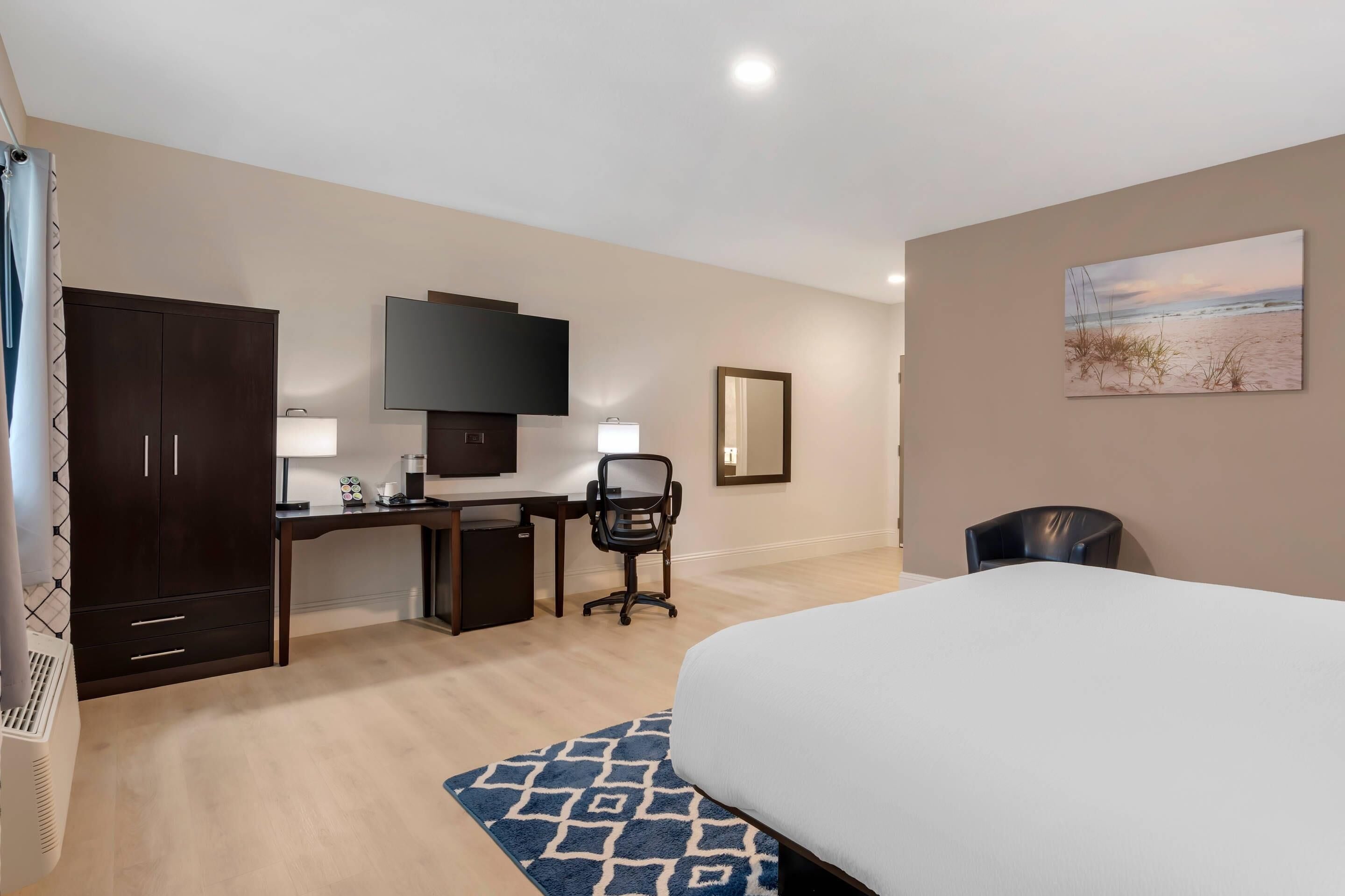 Une chambre d’hôtel équipée d’un lit, d’un bureau, d’une chaise, d’une armoire, d’une télévision et d’œuvres d’art accrochées au mur.