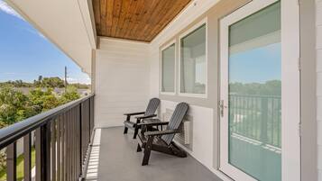 A balcony with two Adirondack chairs, a wooden ceiling, and a view of greenery and buildings.