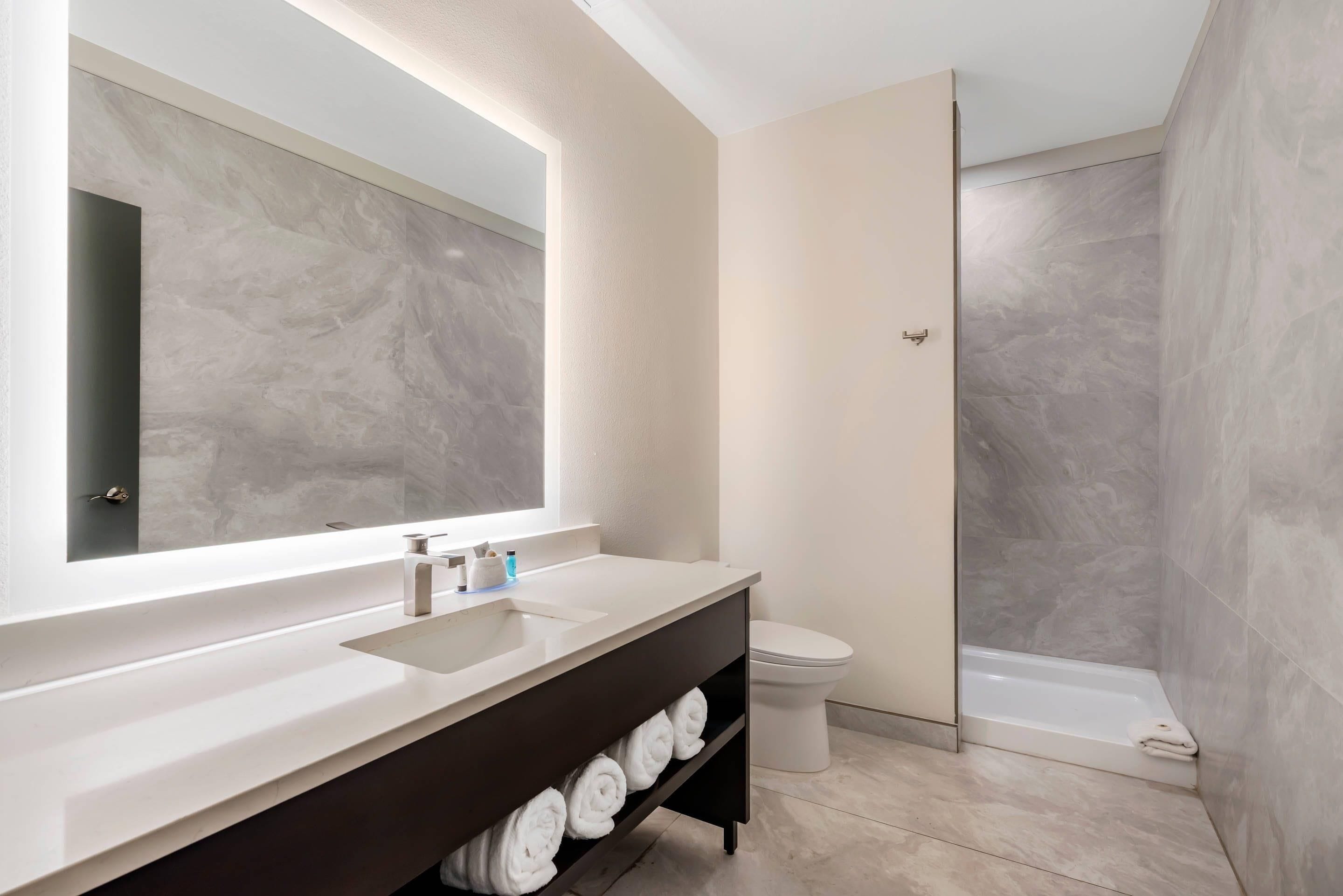 A modern bathroom with a large mirror, a sink, a toilet, and a shower.