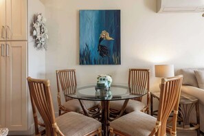 Un comedor con una mesa de vidrio rodeada de sillas de mimbre, un cuadro en la pared y un pequeño vehículo decorativo sobre la mesa.