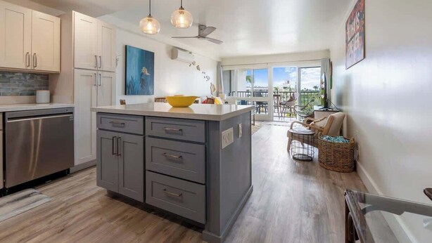 Een moderne keuken met grijze kastjes, een centraal kookeiland, hanglampen en uitzicht op een balkon.