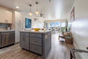 Une cuisine moderne avec des meubles gris, un îlot central, des luminaires suspendus et une vue sur un balcon.