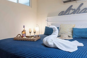 Un lit avec une couverture bleue à motifs, une serviette blanche et un panier contenant une bouteille et des verres.