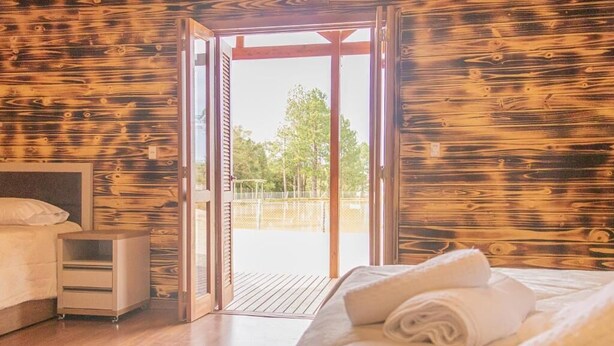 Ein Schlafzimmer mit Holzboden, einem Bett, einem Nachttischwagen und einer Schiebeglastür, die zu einem Außenbereich führt.