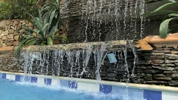Una piscina con una cascada rodeada de muros de piedra y follaje.