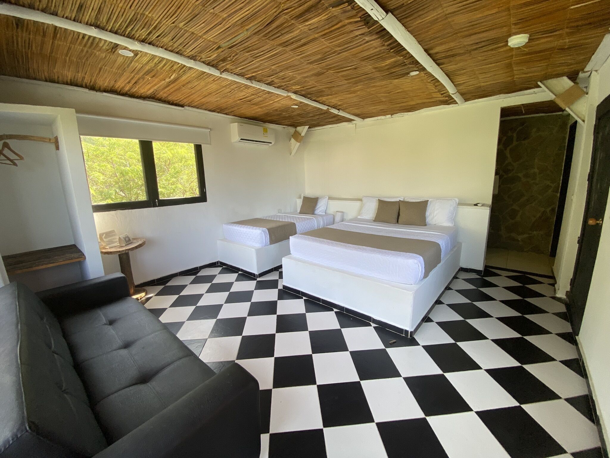 A room with a checkered floor, a bed with two pillows, a small table, and a couch.