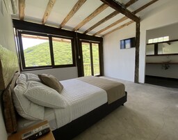 Un dormitorio con cama, ventana con vista a follaje, televisor y baño con lavabo.