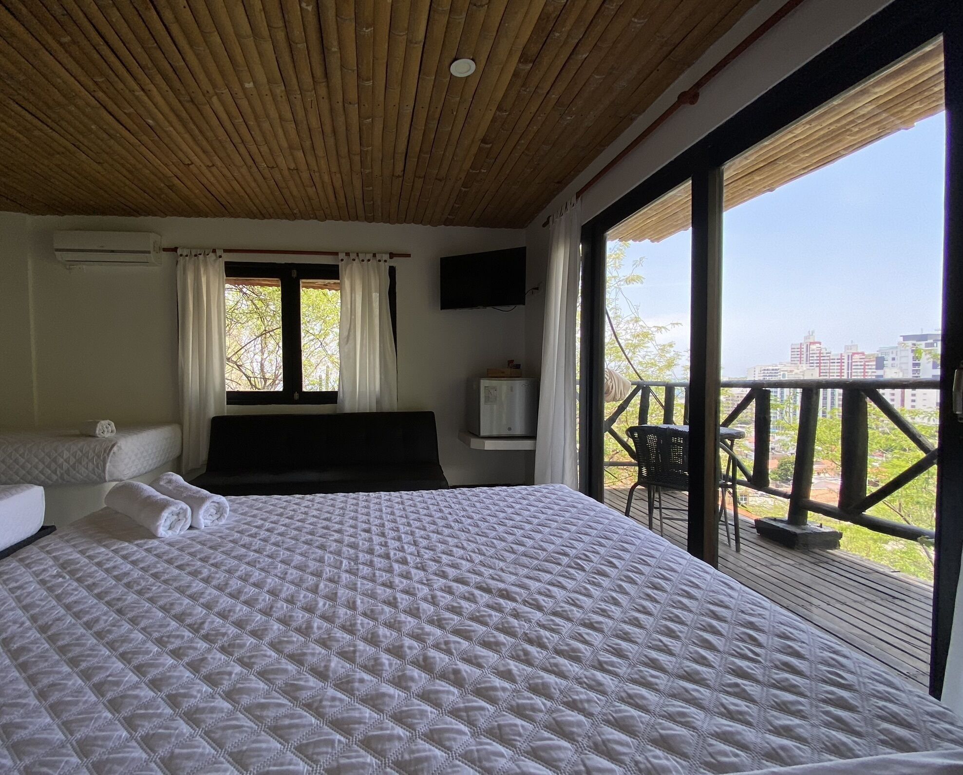 A bedroom with a large bed, a smaller bed, a TV, and a balcony with a view of buildings.