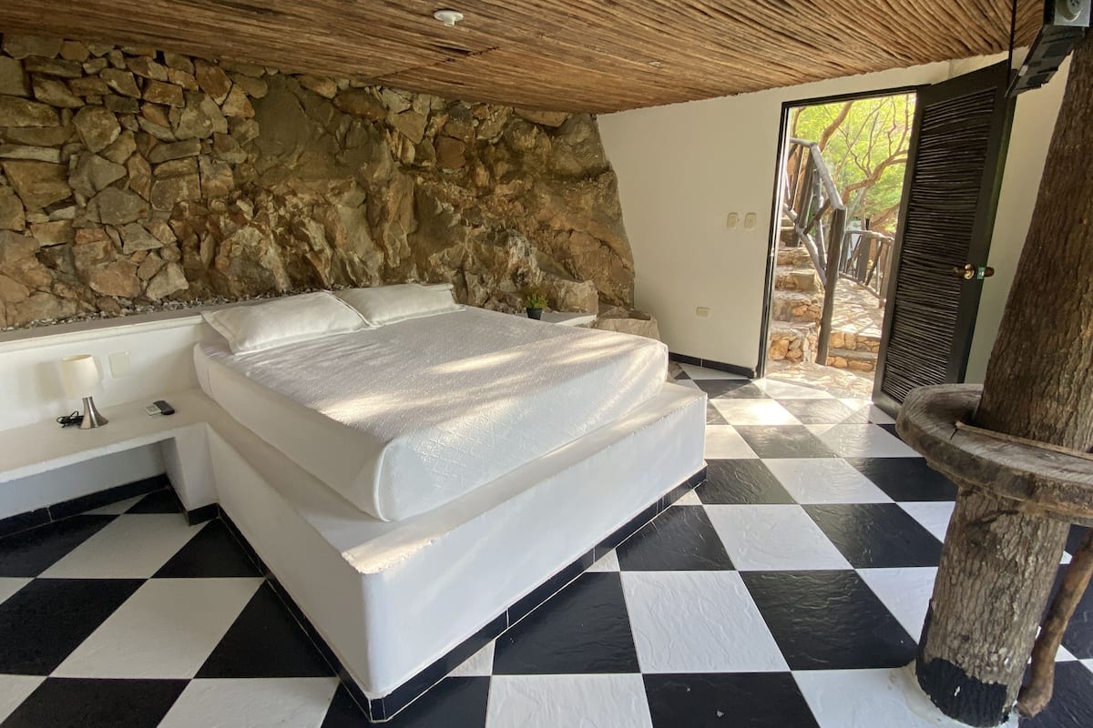 Un dormitorio con pared de piedra, suelo a cuadros, cama y puerta que da al exterior.