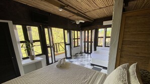Un dormitorio con una cama grande, un ventilador de techo y vistas a un área exterior a través de puertas abiertas.