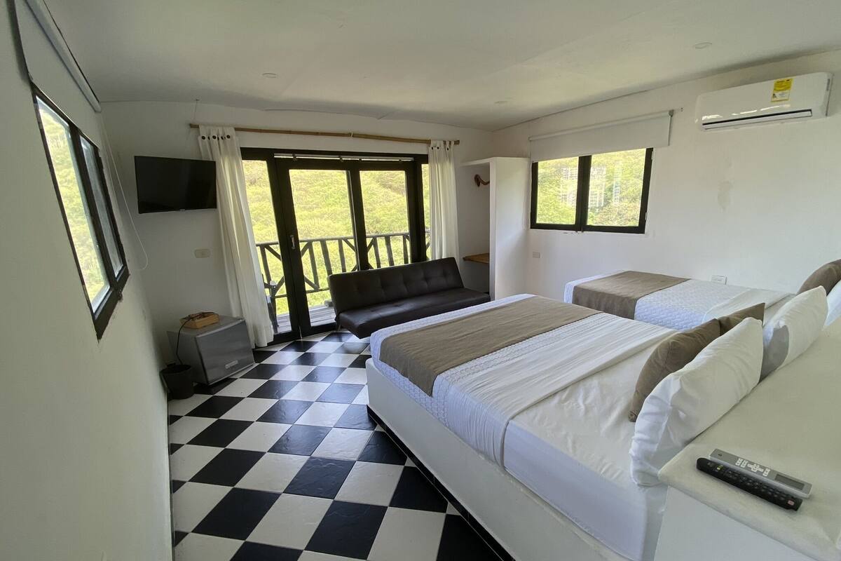 Una habitación de hotel con piso a cuadros, dos camas, un televisor y un balcón con vistas.