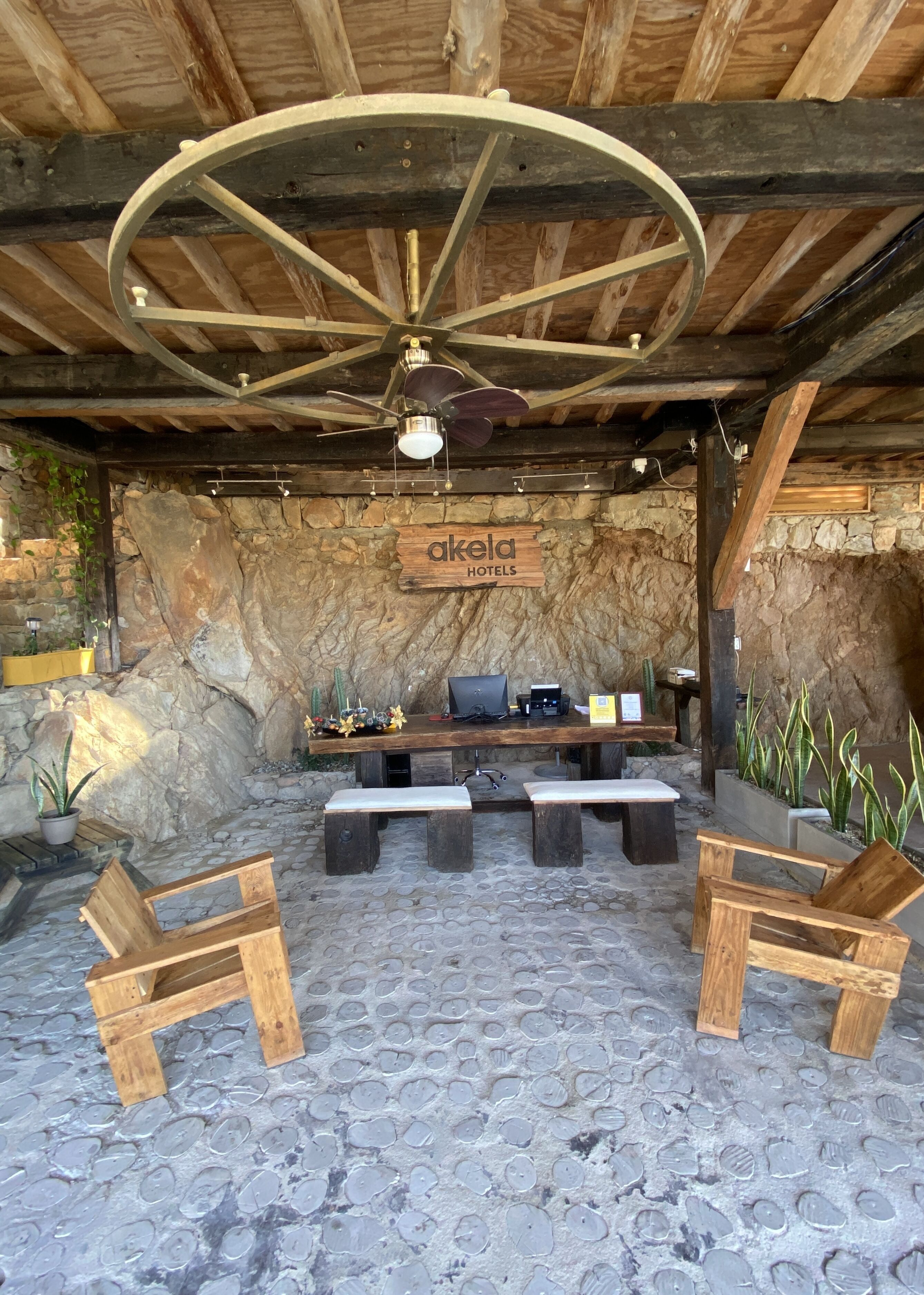 A rustic outdoor seating area with stone walls, wooden furniture, and a ceiling fan.