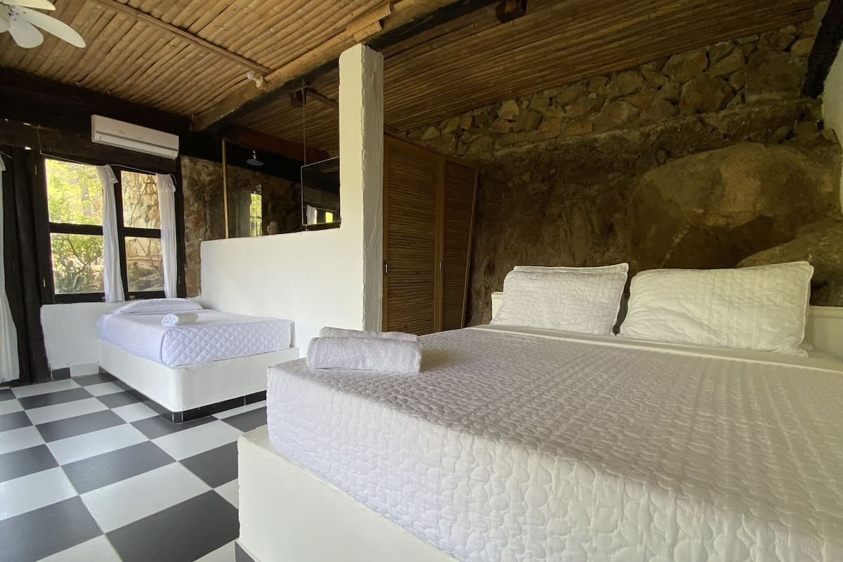 Un dormitorio con suelo a cuadros, una cama grande, dos camas más pequeñas y una pared de piedra.