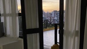 Un umbral abierto que da a un balcón con piso a cuadros, cortinas blancas y vistas de la ciudad.