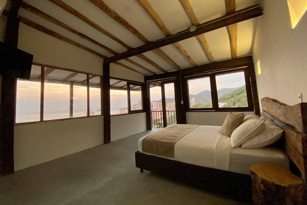 Un dormitorio con una cama grande, vigas de madera y vistas a la ciudad y las montañas.