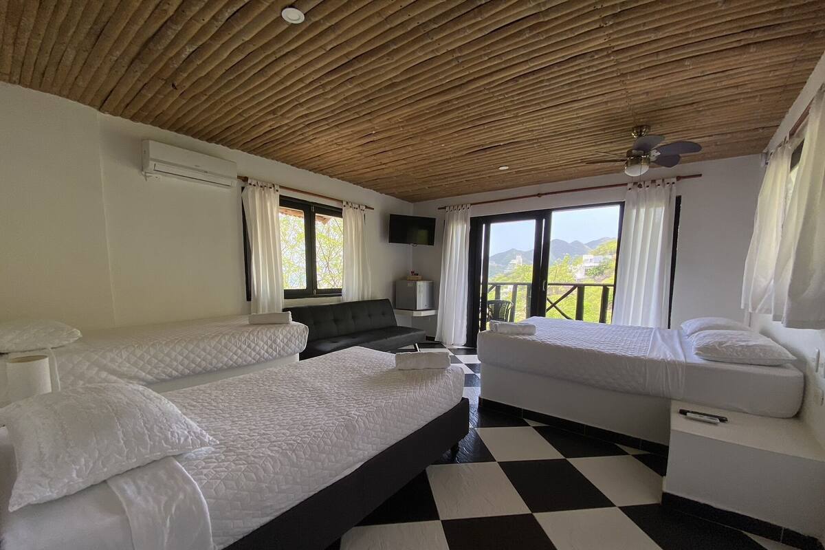 Habitación de hotel con dos camas, piso a cuadros, ventilador de techo y vista al exterior.