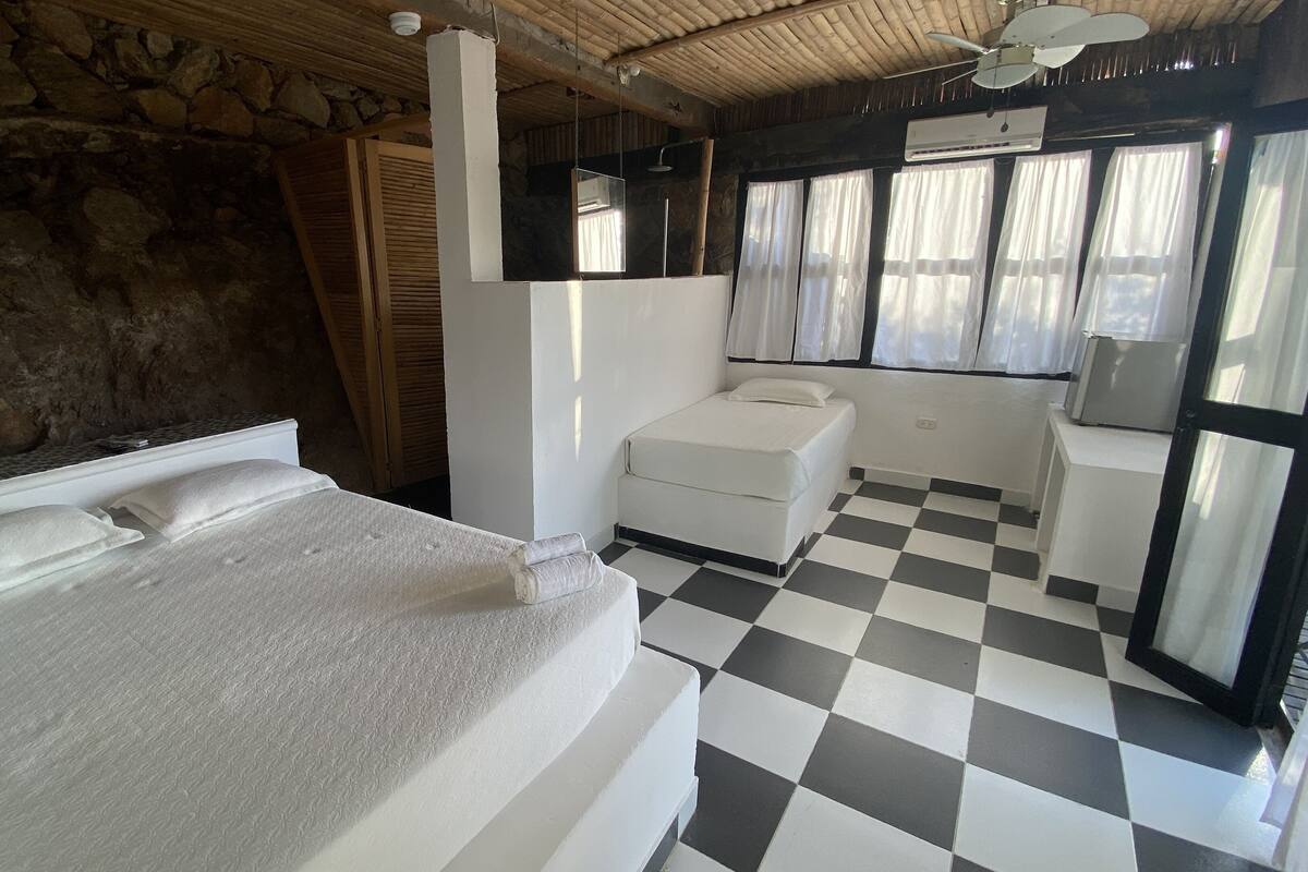 Una habitación con cama, una mesita, una silla y un ventanal con cortinas.