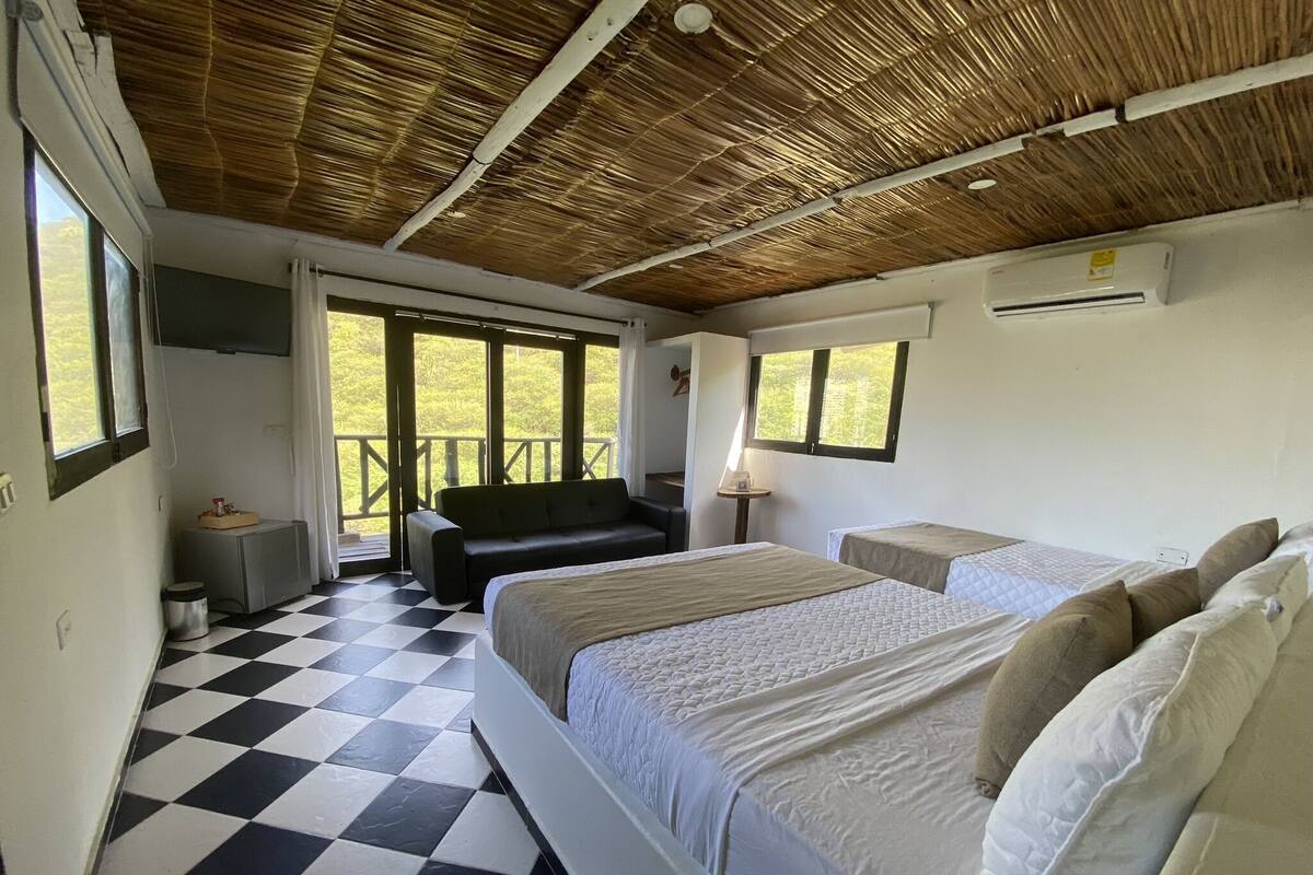 Una habitación con suelo de cuadros, una cama con ropa de cama blanca, un sofá y un balcón con vistas.
