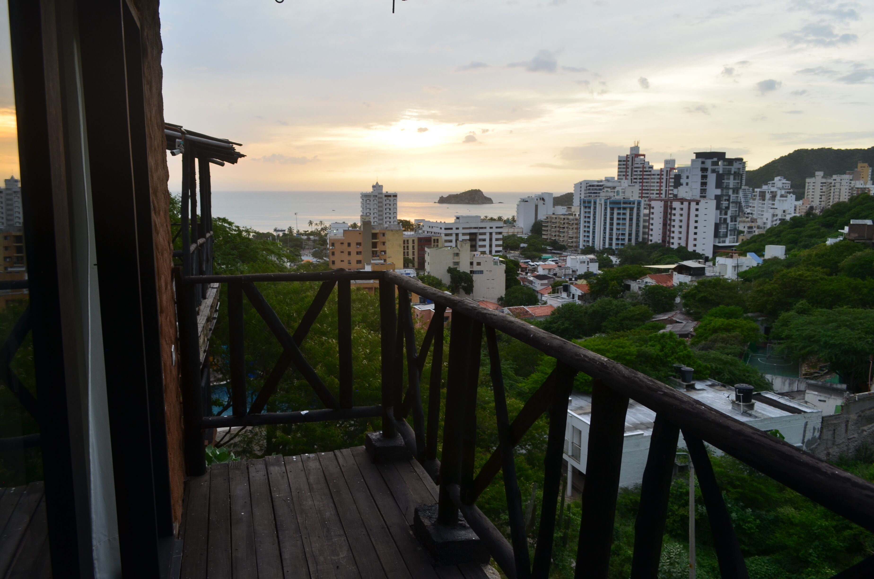 A wooden balcony with a railing overlooking a cityscape during sunset.