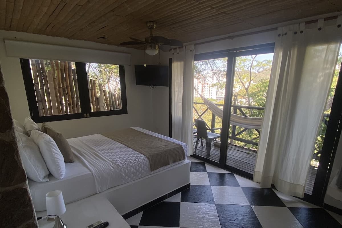 Un dormitorio con suelo a cuadros, una cama, un televisor y un balcón con una hamaca.