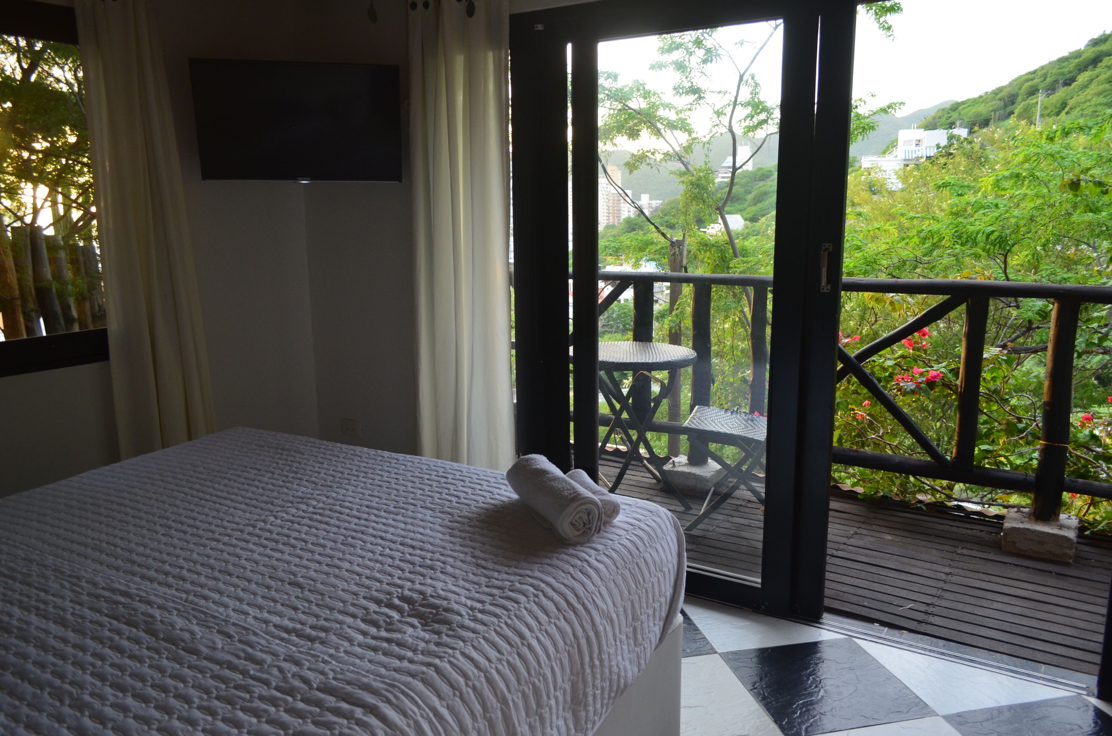 Habitación de hotel con cama, televisión montada en la pared y balcón con mesa y sillas.