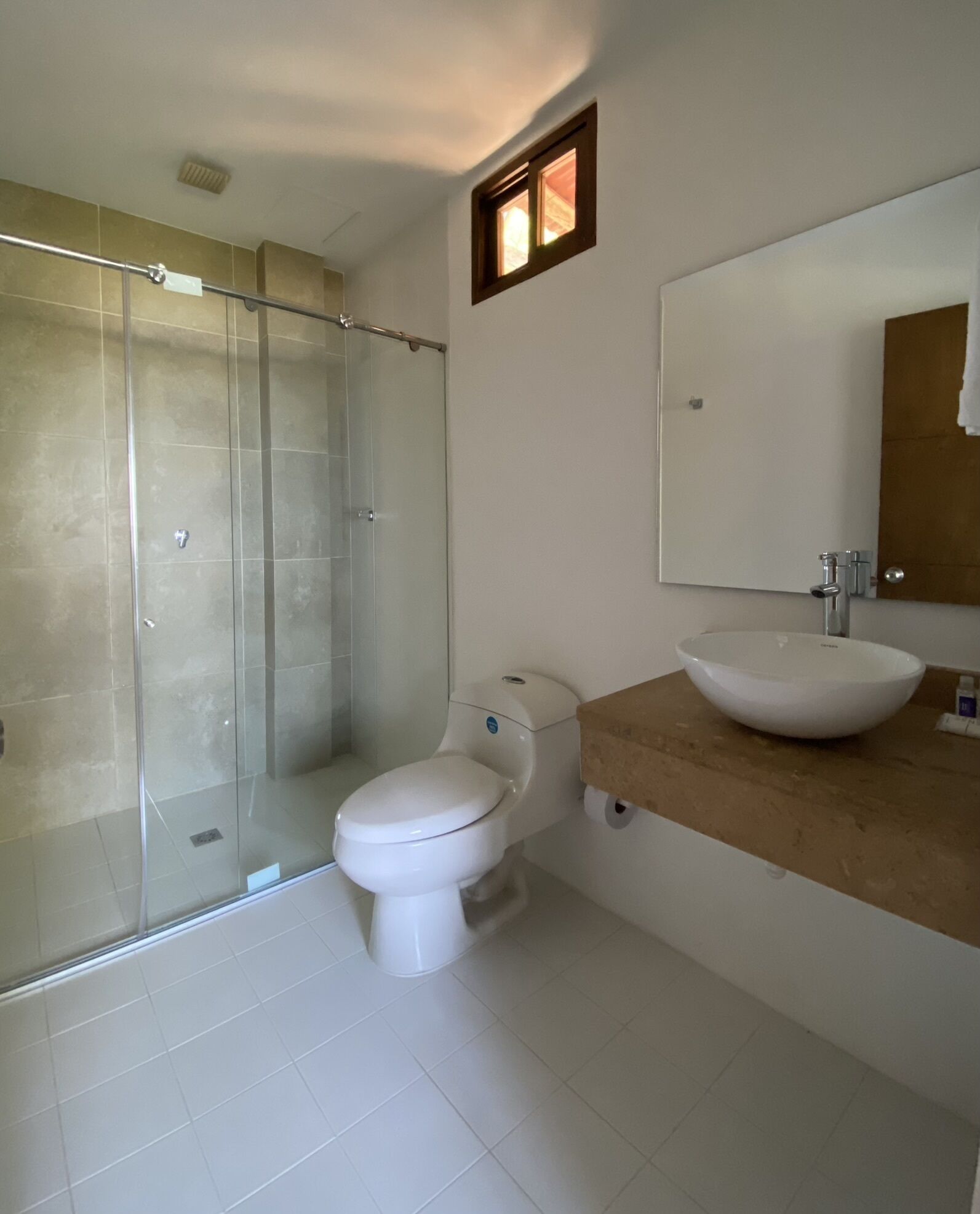 Een badkamer met een glazen douchecabine, toilet, wastafel met spiegel en een handdoek aan de muur.