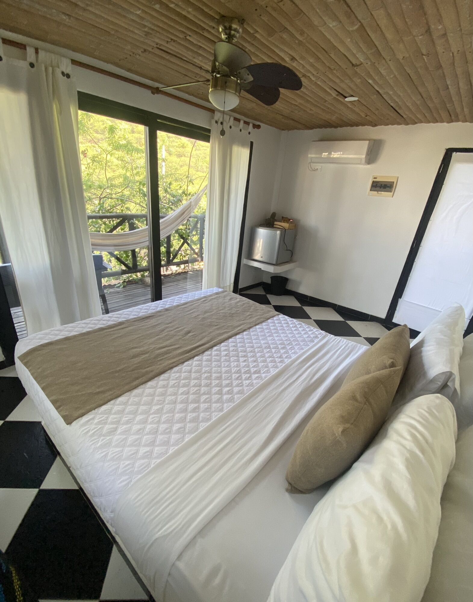 A bedroom with a bed, a ceiling fan, a window with curtains, and a view of greenery outside.