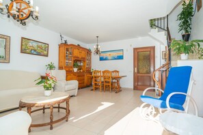 Een woonkamer met een bank, een eettafel met stoelen, een blauwe stoel, een houten kast en een trap met een leuning.