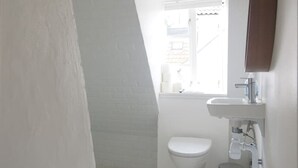 Ein kleines, weißes Badezimmer mit Toilette, Waschbecken und Fenster.