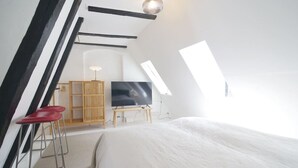 Ein modernes, helles Schlafzimmer im Dachgeschoss mit einem großen Bett, einem Fernseher und einem Holzschrank.