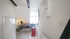 Eine schmale Küche mit einem Kühlschrank, Spüle und einer roten Mülltonne.