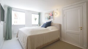 A bedroom with a bed, a door, a window with curtains, and a wall-mounted light fixture. - LBS 3 · Copenhagen Hotel Apartments (København)