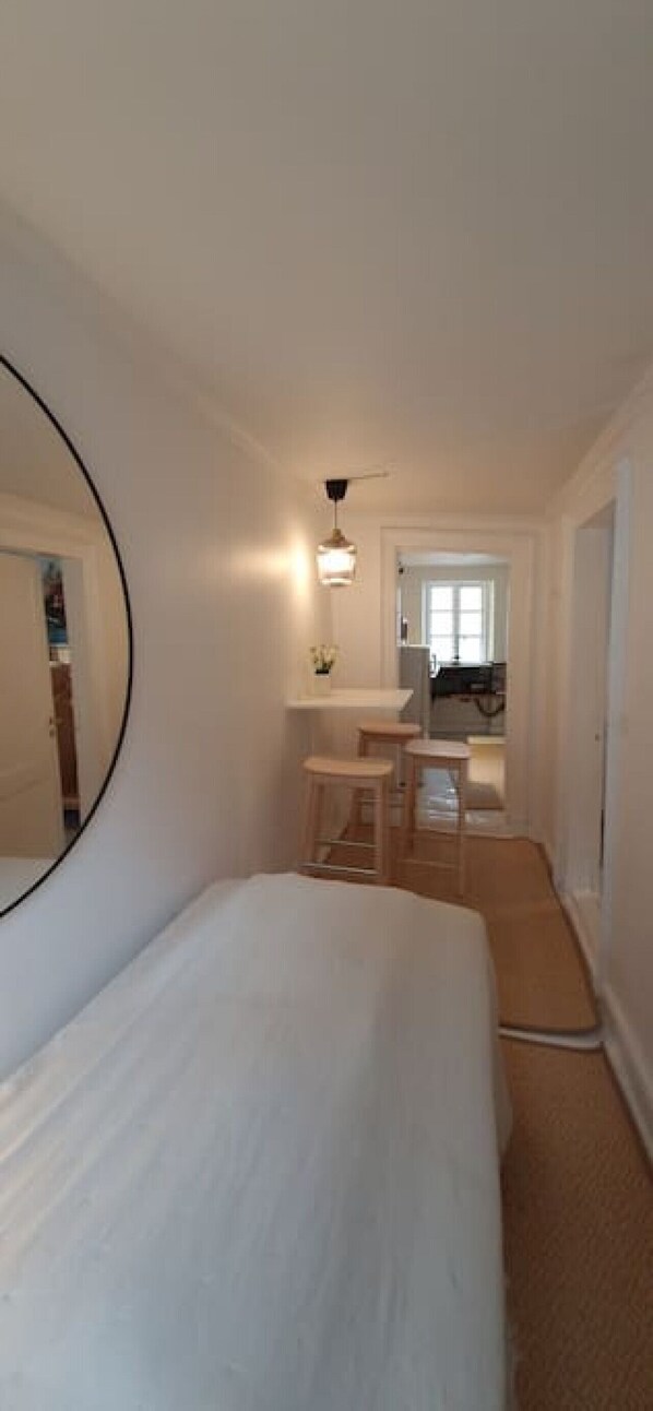 A bedroom with a large bed, a mirror, a small table, and a chair. There is a window with a view of the outside.